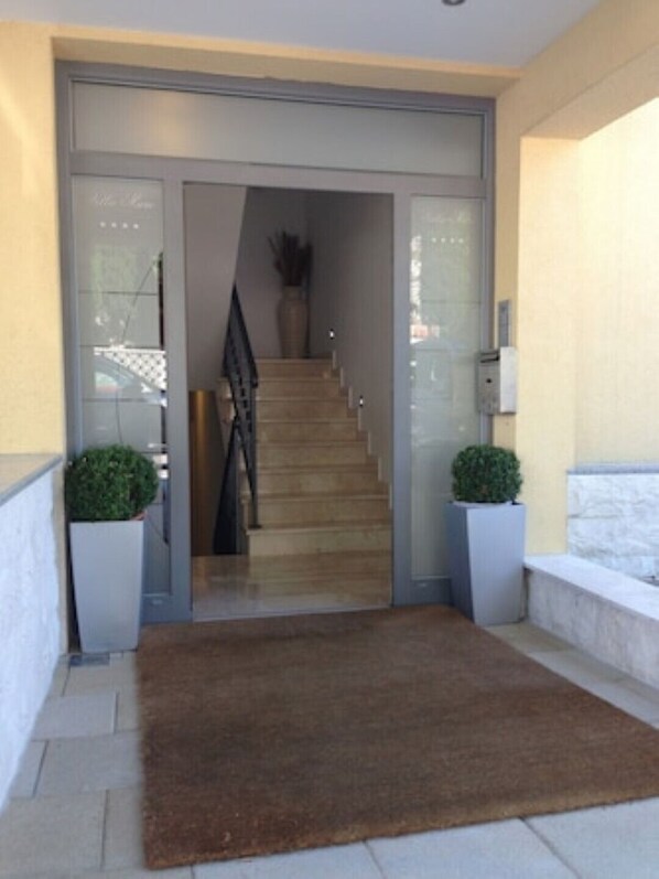 A modern entrance with a glass door, a wooden staircase, and two potted plants.