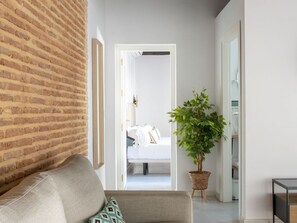 A modern hotel room with a brick wall, a grey sofa, a potted plant, and a bed with white bedding. - Hommyhome Triana Boutique Apartments 004 (Sevilla)