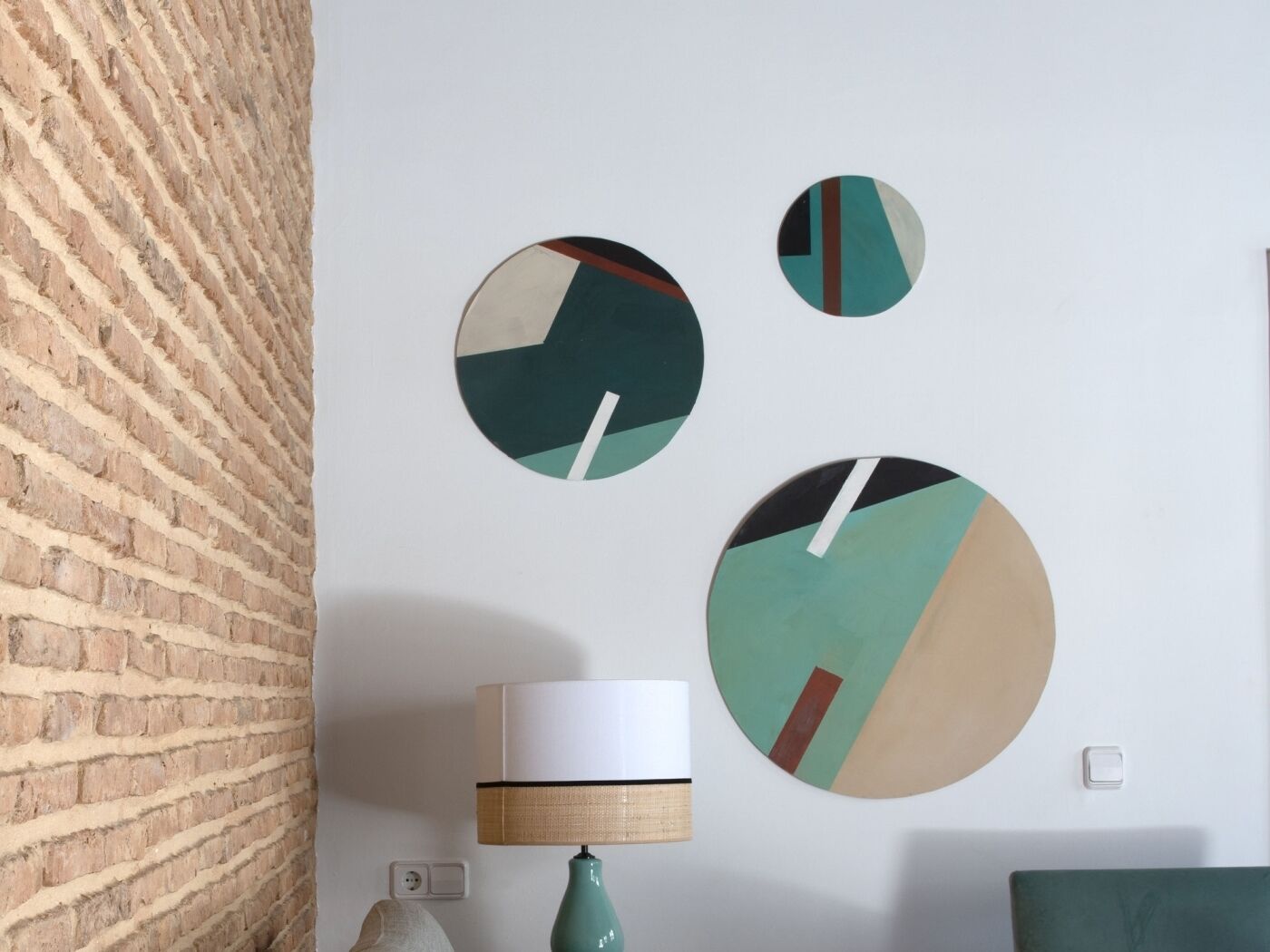 Une pièce avec un mur en briques, une lampe et trois œuvres d’art murales de forme circulaire.