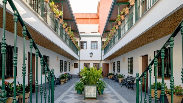 Ein Innenhof mit Schachbrettmuster-Boden, grünen Geländern, Blumentöpfen und Bänken.