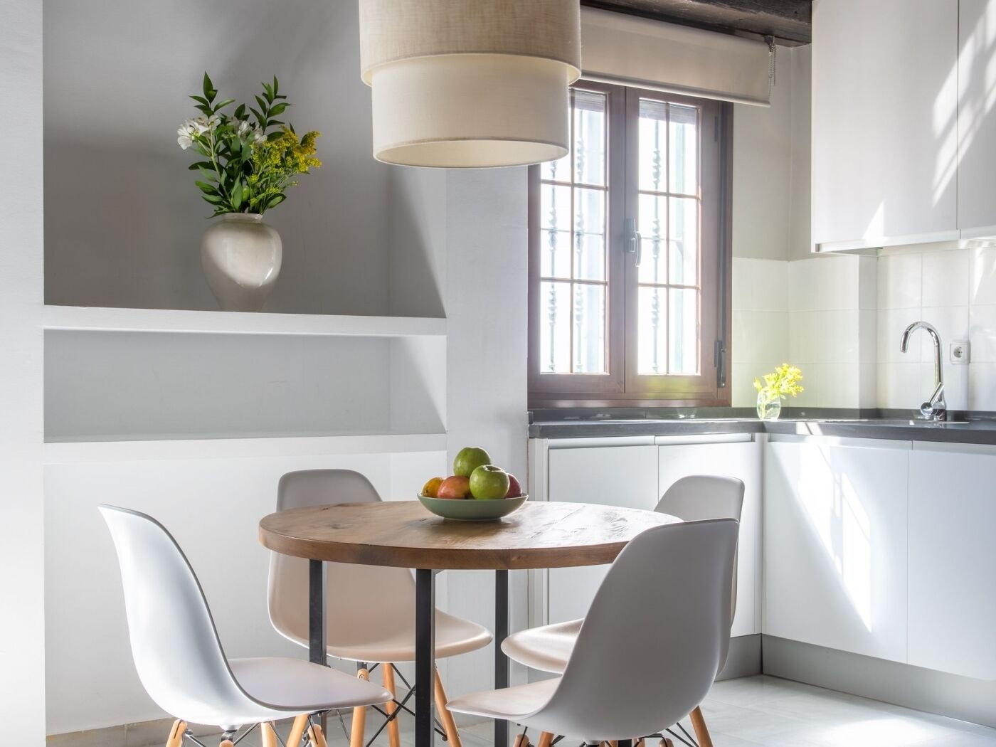 A modern kitchen with white cabinets, a round wooden table, and a hanging light fixture.