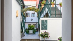 Un callejón estrecho con una escalera que lleva a un edificio. Hay plantas en macetas y un cartel con números de habitaciones.