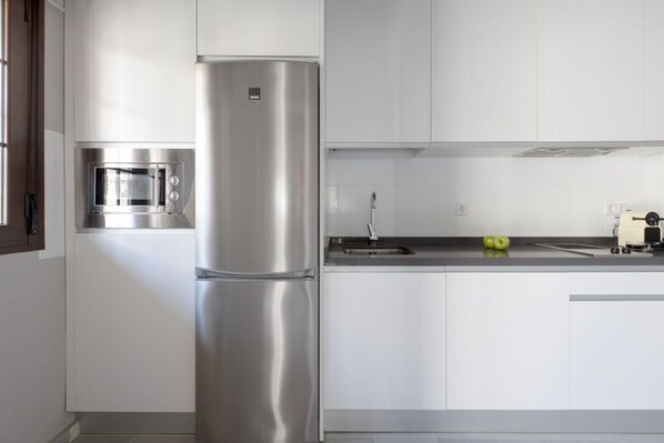A modern kitchen with white cabinets, a stainless steel refrigerator, a built-in microwave, and a sink.