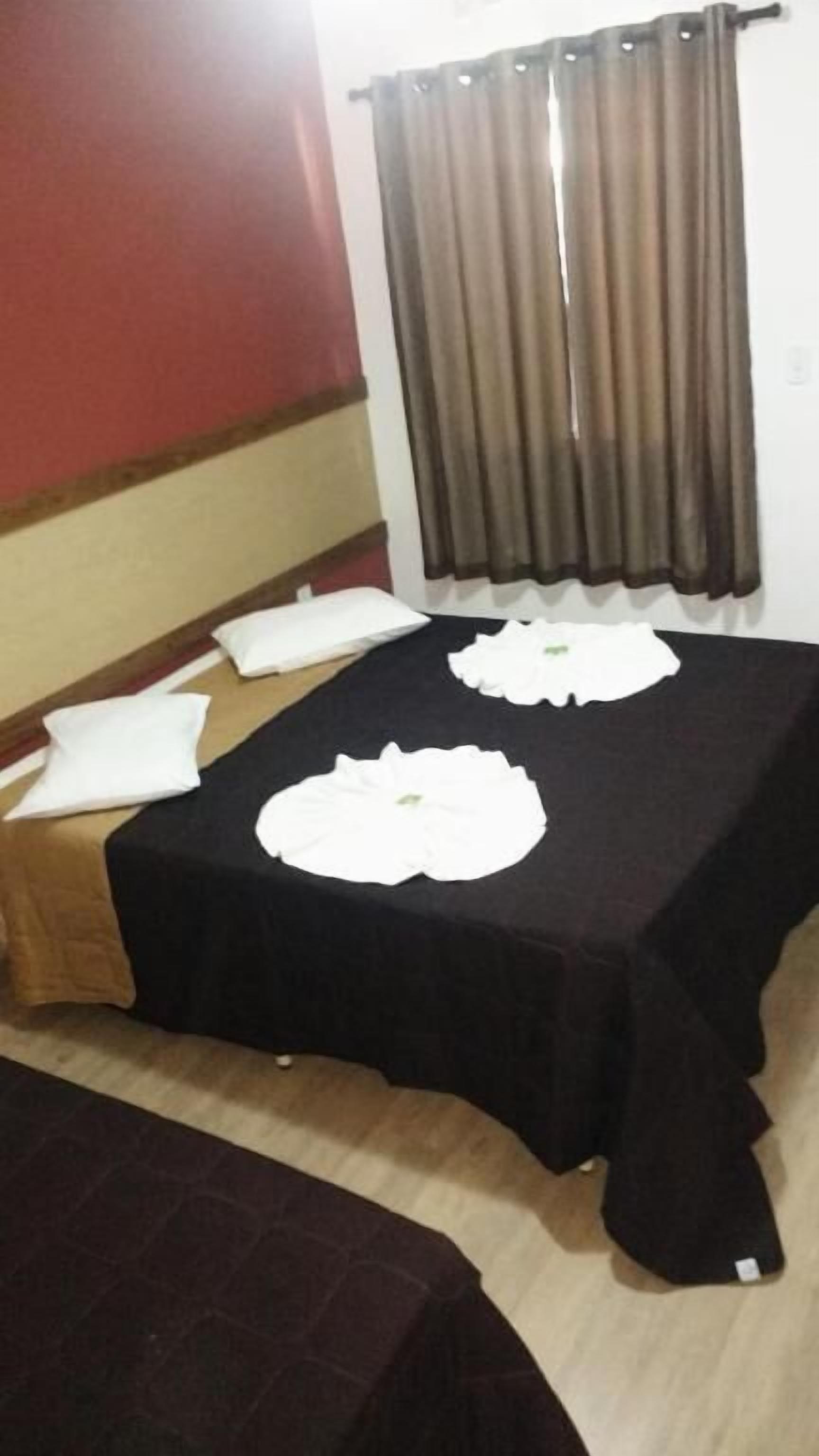 A hotel room with a bed, a table with white placemats, and a window with curtains.