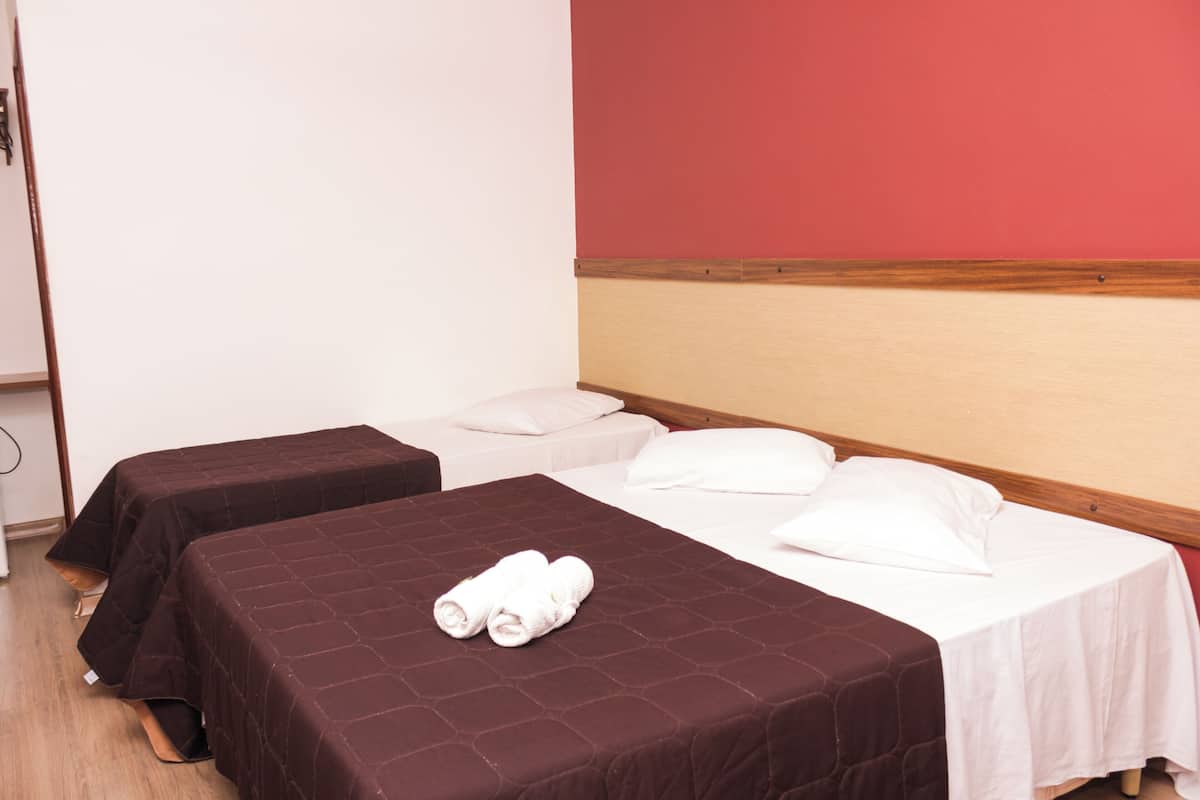 A hotel room with two beds, one with a brown bedspread and the other with a white bedspread. There are towels on the brown bedspread.