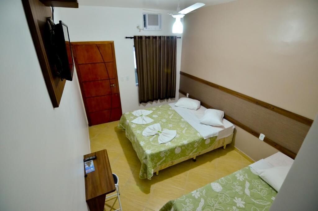 A small, clean room with two beds, a wooden door, a small table, and a TV mounted on the wall.