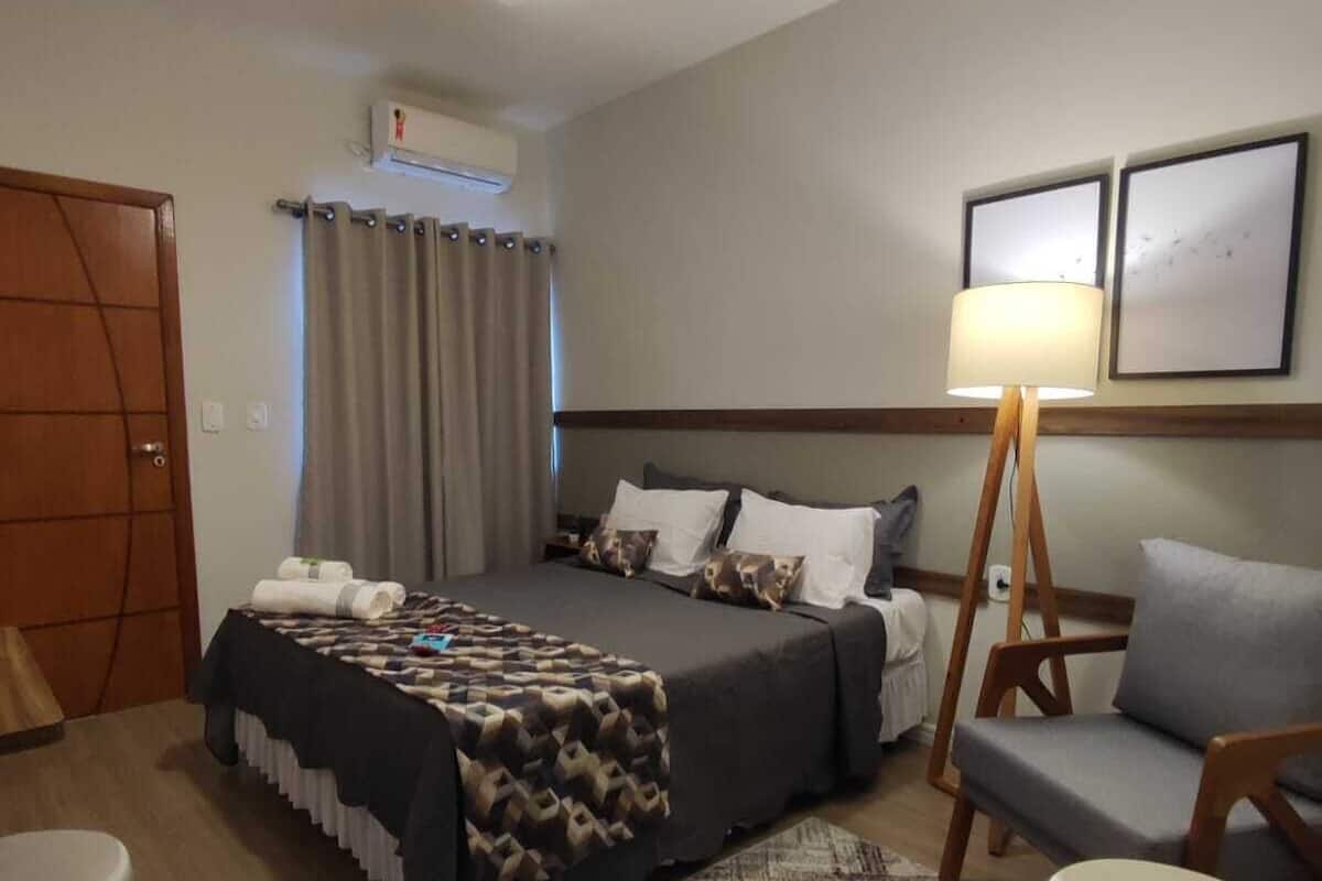 A hotel room with a bed, a desk, a chair, a lamp, and a ceiling fan.