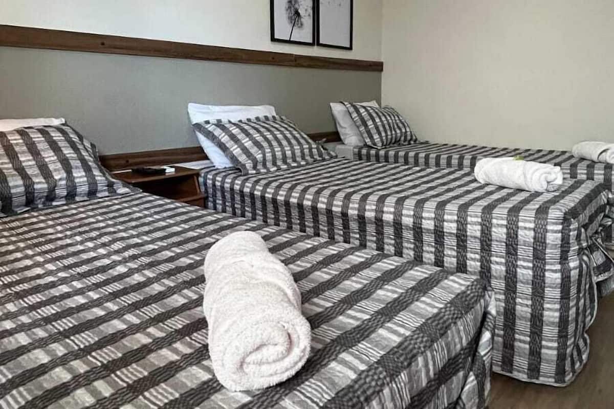 A hotel room with two single beds, each with striped bedding and a rolled towel on the bed. There is a wooden headboard, a framed picture on the wall, and a ceiling light.