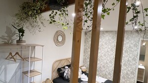 Une chambre à coucher avec un lit, une chaise en bois, une étagère avec des cintres et une plante suspendue.