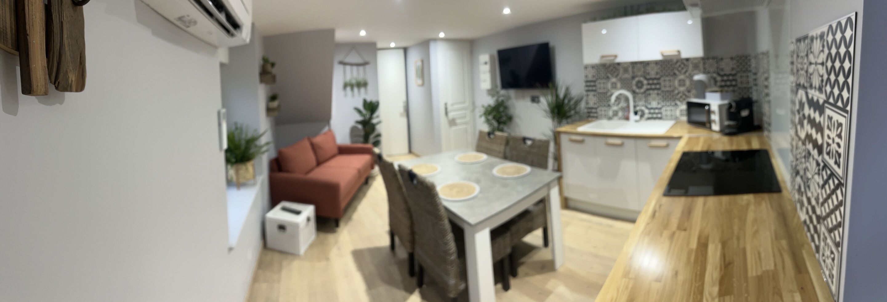 A modern kitchen with a dining area, a red sofa, and a TV mounted on the wall.