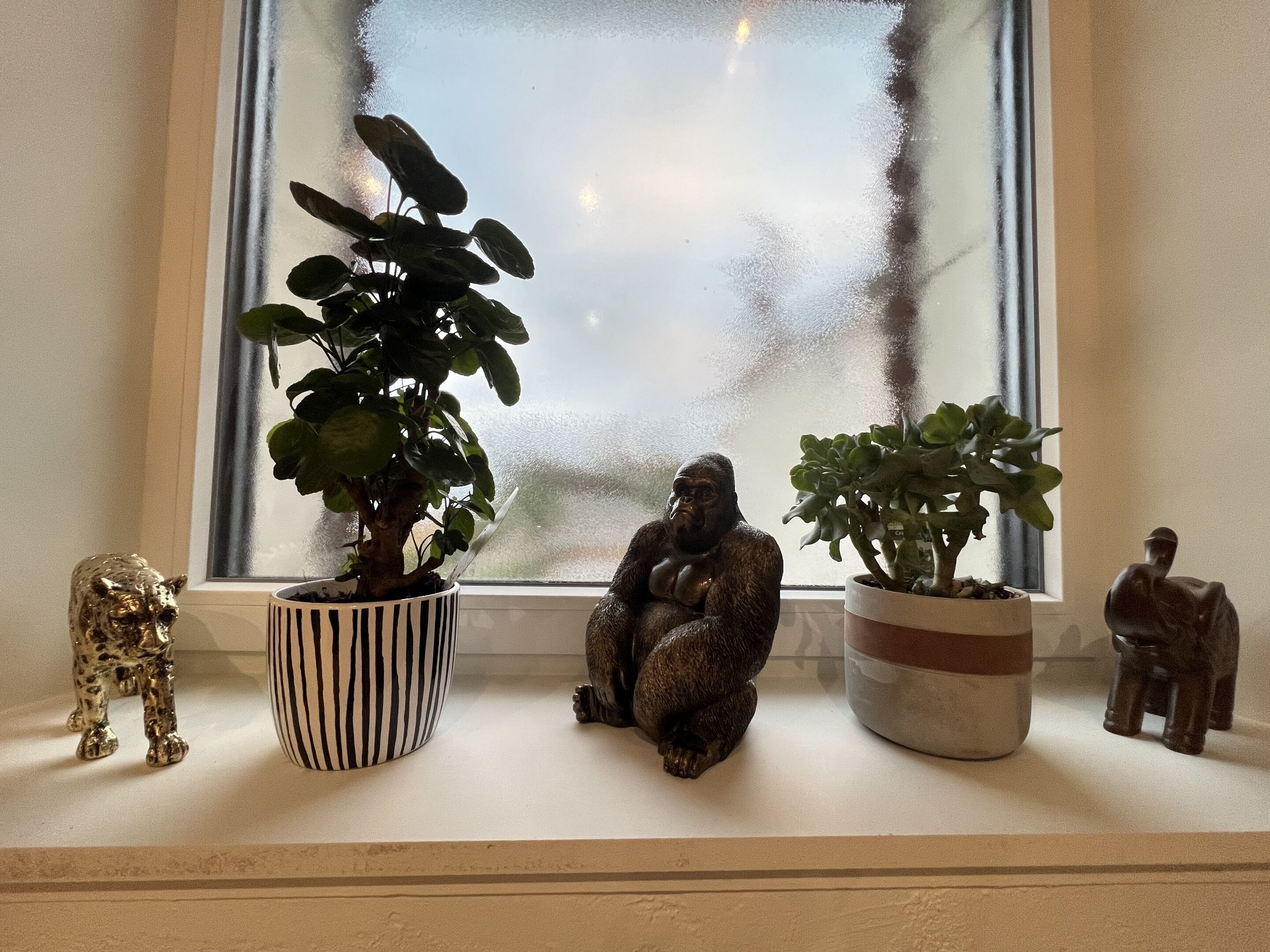 A window sill with three potted plants and two animal figurines.