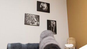 Un lit bien fait, avec une serviette pliée, une table de chevet sur laquelle se trouve une boîte de mouchoirs, et trois photographies d’animaux encadrées accrochées au mur.