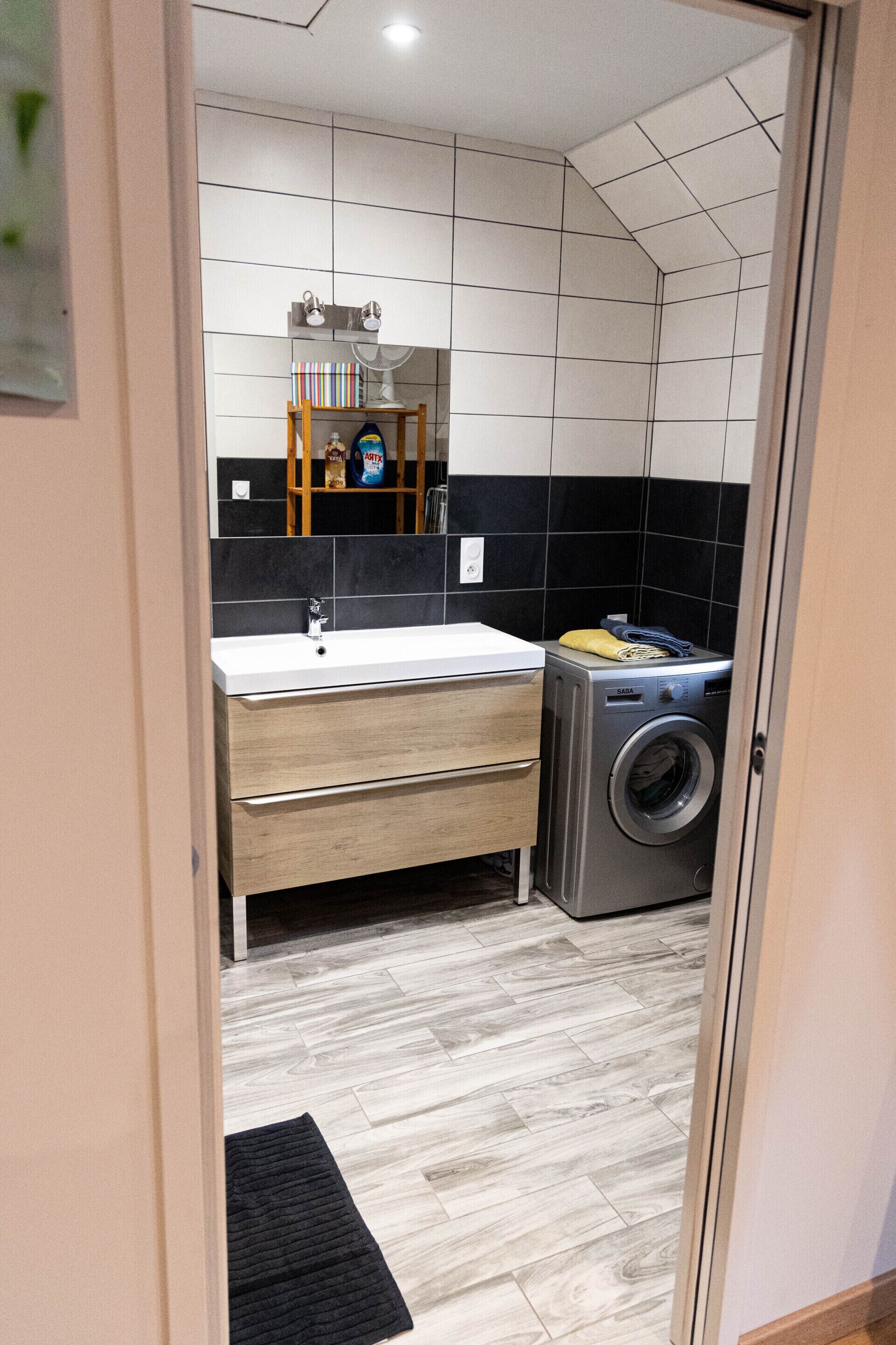 Un baño moderno con lavamanos, espejo y lavadora.