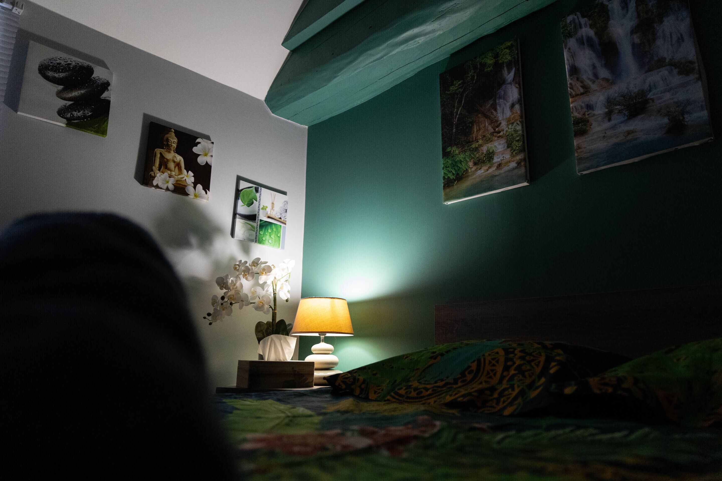 Un dormitorio con cama, mesita de noche, lámpara y decoración en la pared, incluyendo una estatua de Buda y una pintura de cascada.