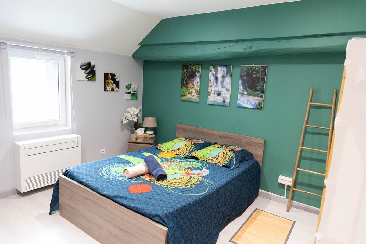 Ein Schlafzimmer mit Bett, Fenster, Nachttisch und einer Wand mit Bildern.