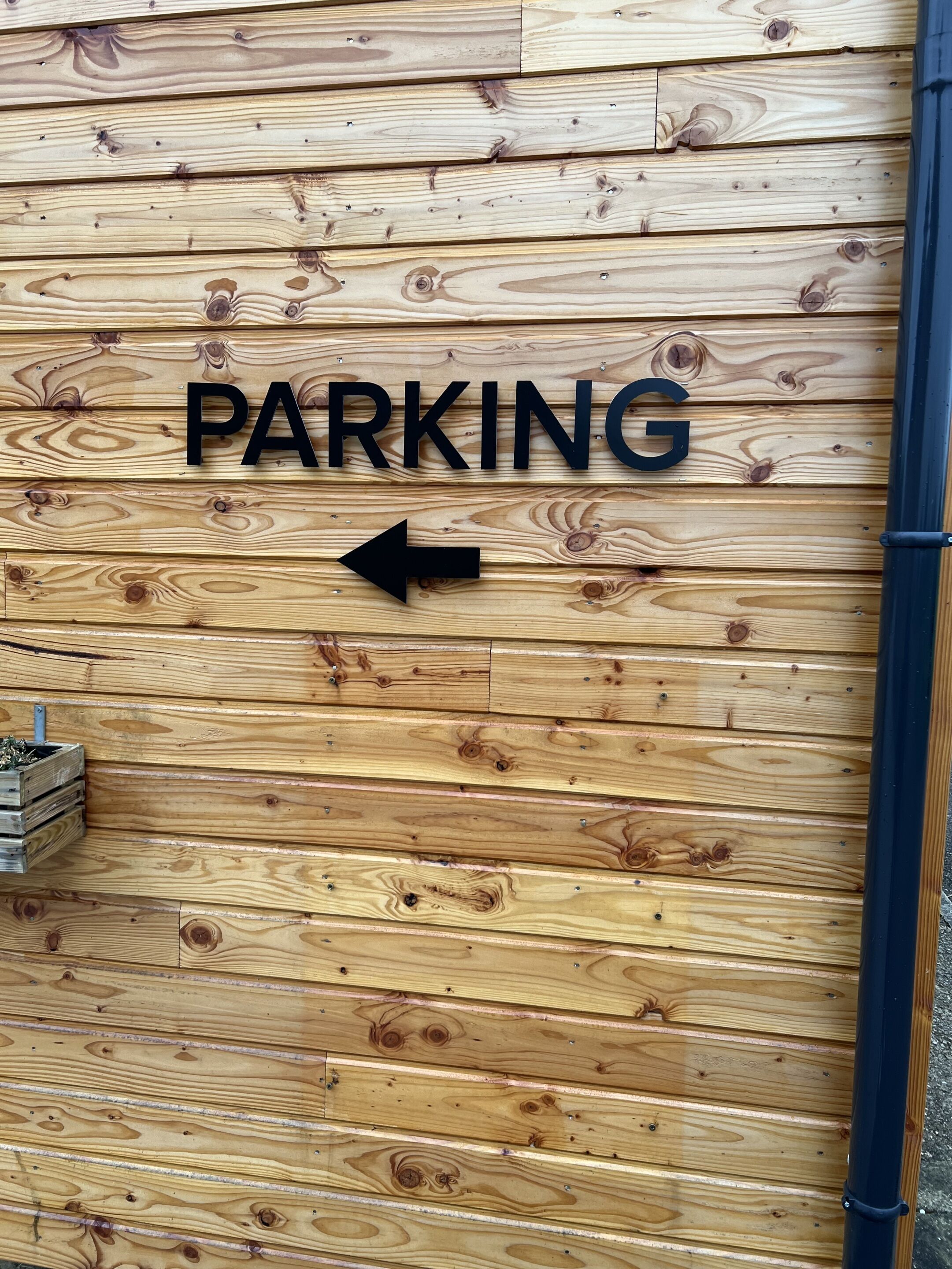 A wooden wall with a sign that reads "PARKING" and an arrow pointing to the left.