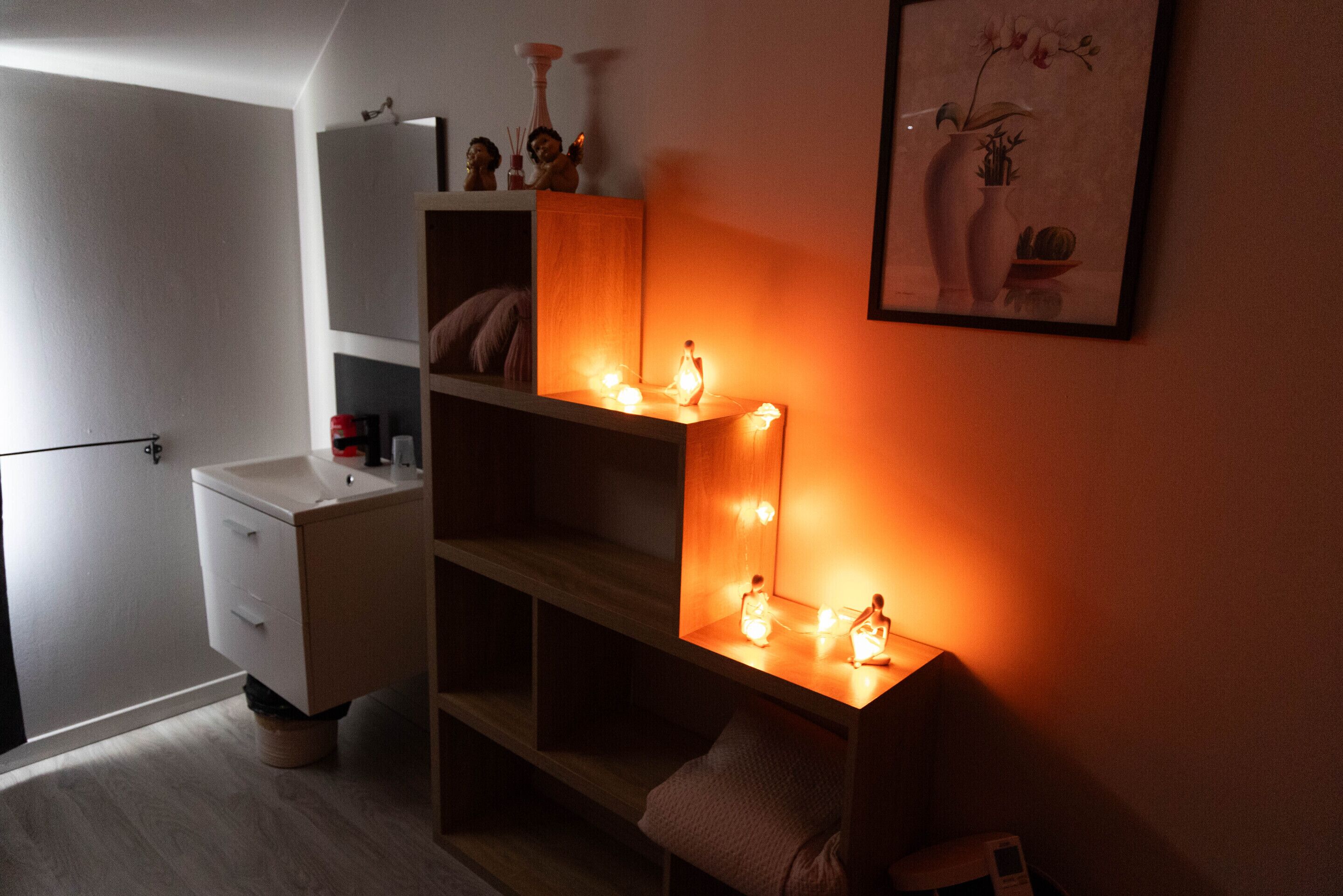 Una habitación pequeña y tenuemente iluminada, con tocador, estanterías y un espejo con luces.