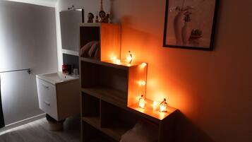 Una habitación pequeña y tenuemente iluminada, con tocador, estanterías y un espejo con luces.