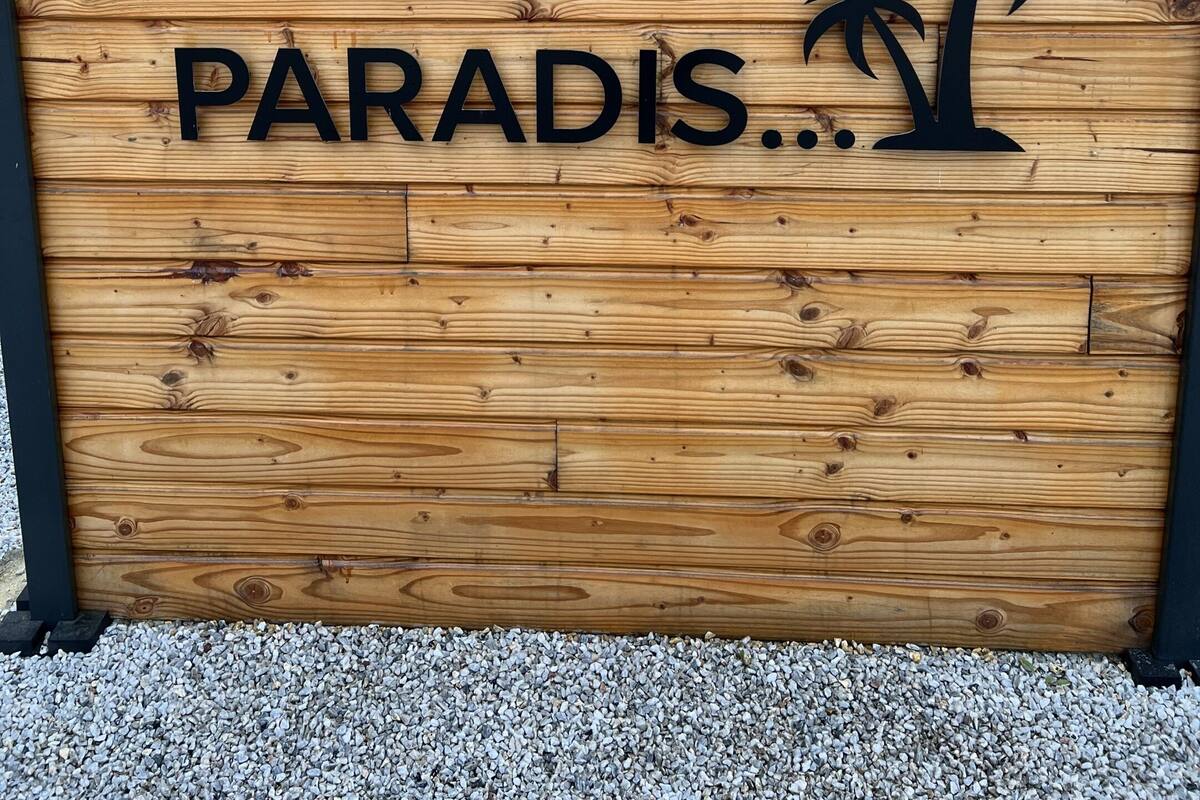 Ein hölzernes Schild mit der Aufschrift 'UN P'TIT COIN DE PARADIS' und einem Palmen-Symbol.