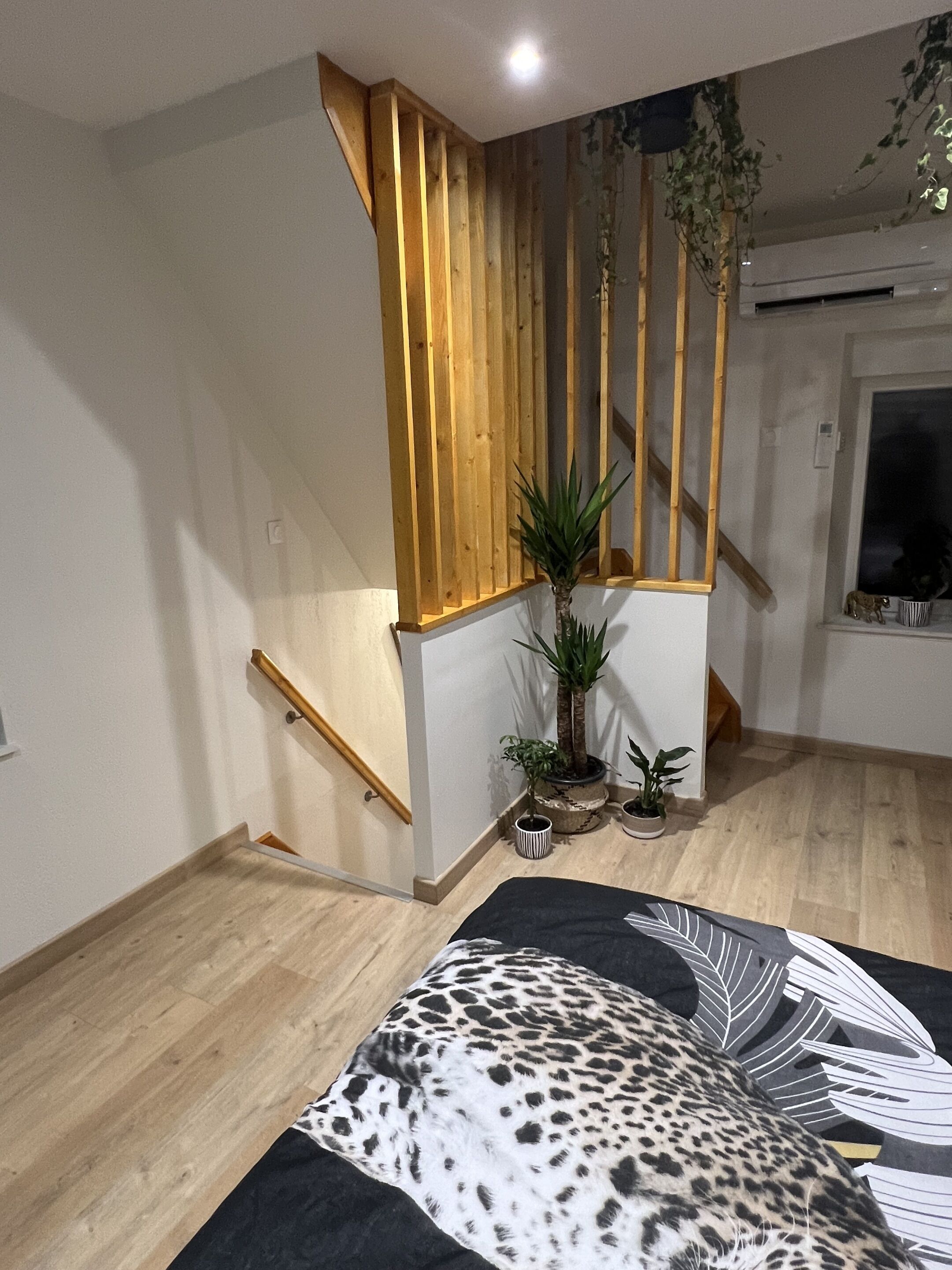 Un escalier avec des rampes en bois, une plante en pot et un tapis à motifs noir et blanc sur le sol.