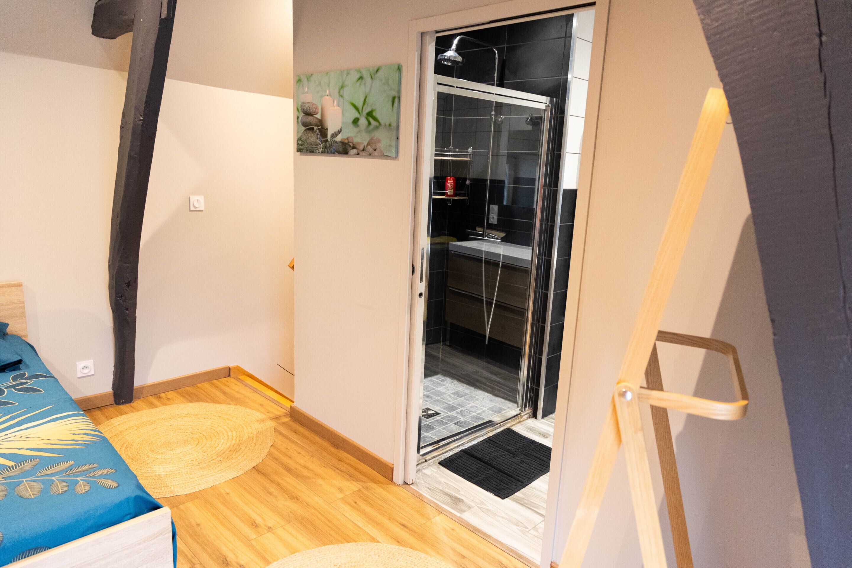 Una habitación pequeña y funcional con cama, zona de ducha y acceso a un baño.