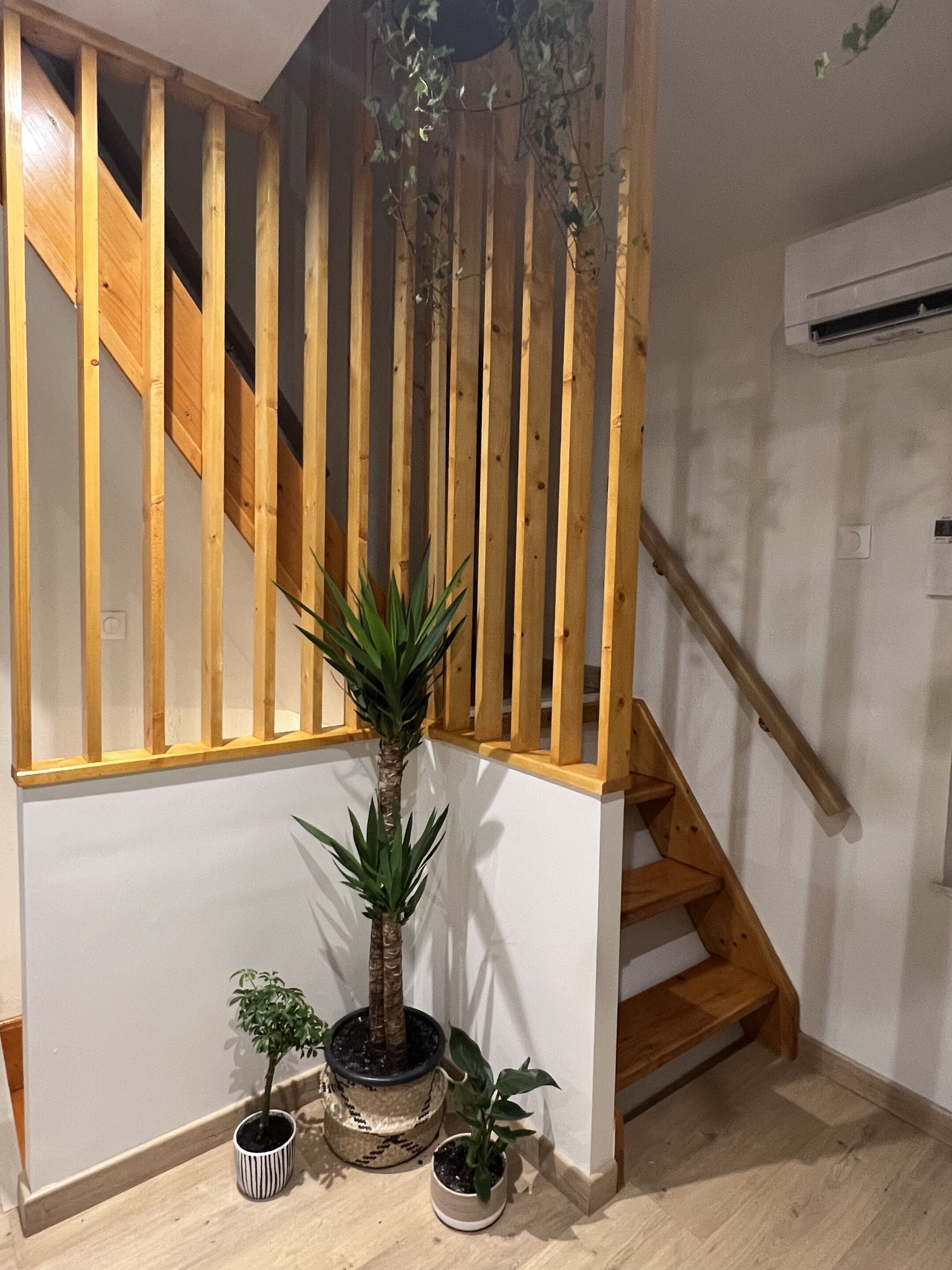 Un escalier avec des rampes en bois, une plante en pot et un petit banc.