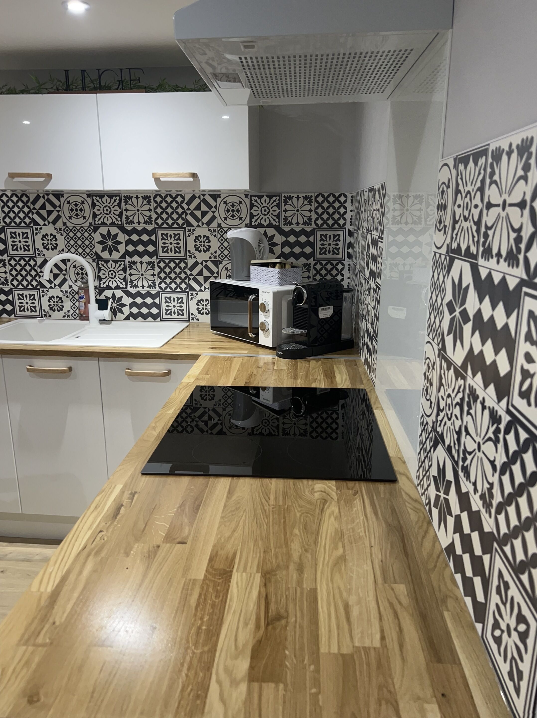 A kitchen with patterned tiles, a microwave, a coffee maker, and wooden cabinets.