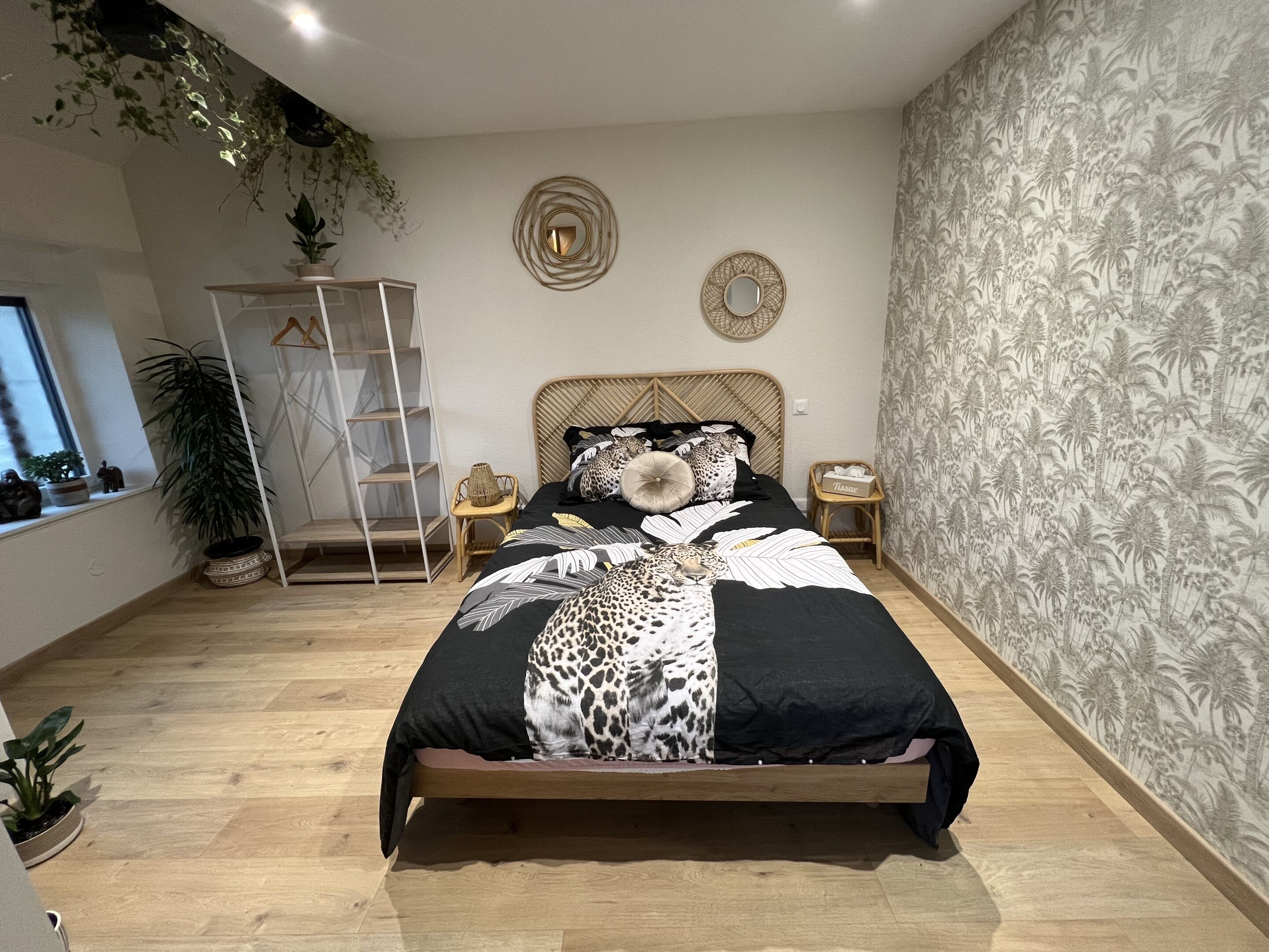 Un dormitorio con una cama, una mesita de noche, un espejo en la pared, un estante y una ventana.