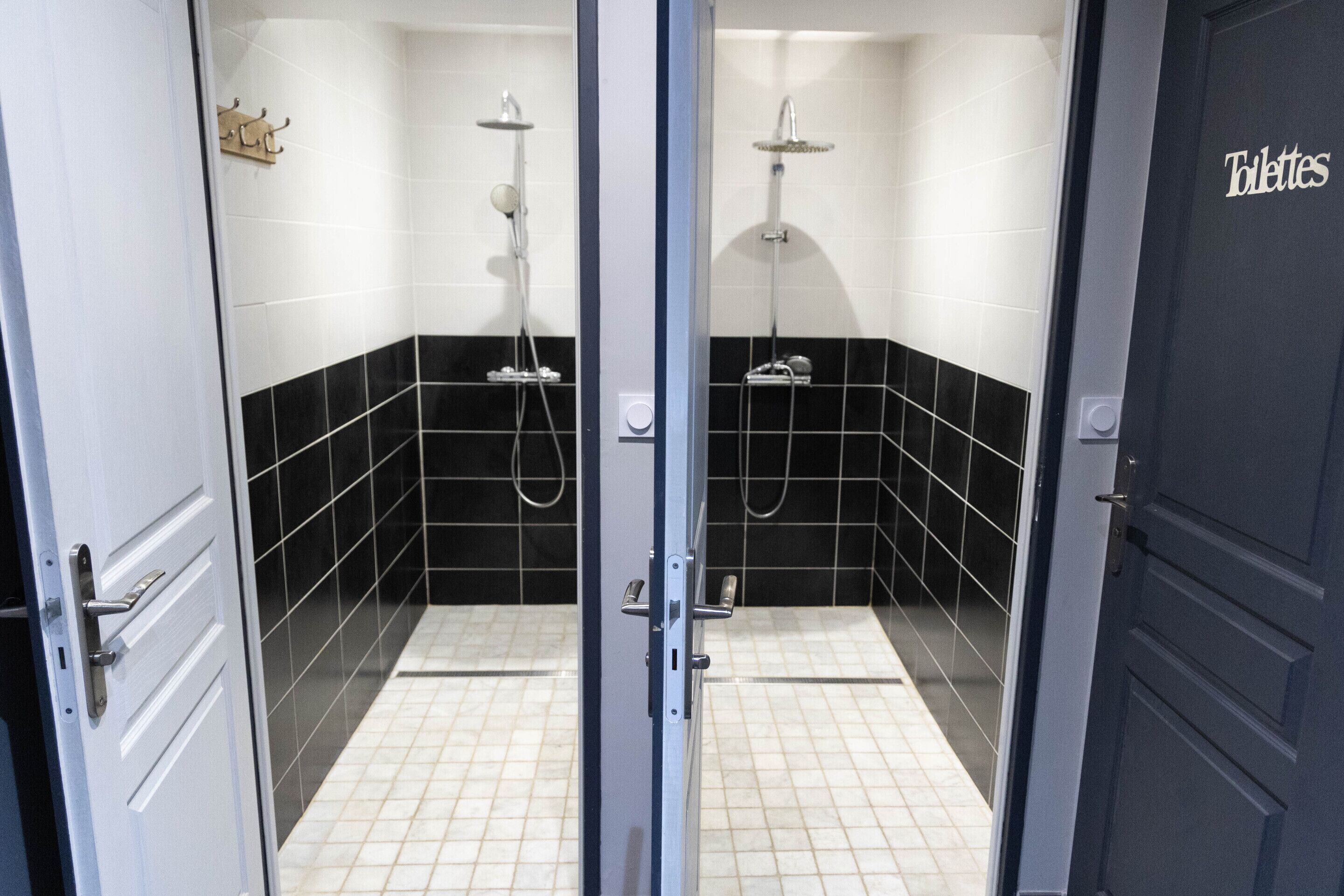 Een badkamer met twee douchecabines, wanden betegeld in zwart en wit, en een deur met de tekst 'Toilettes'.
