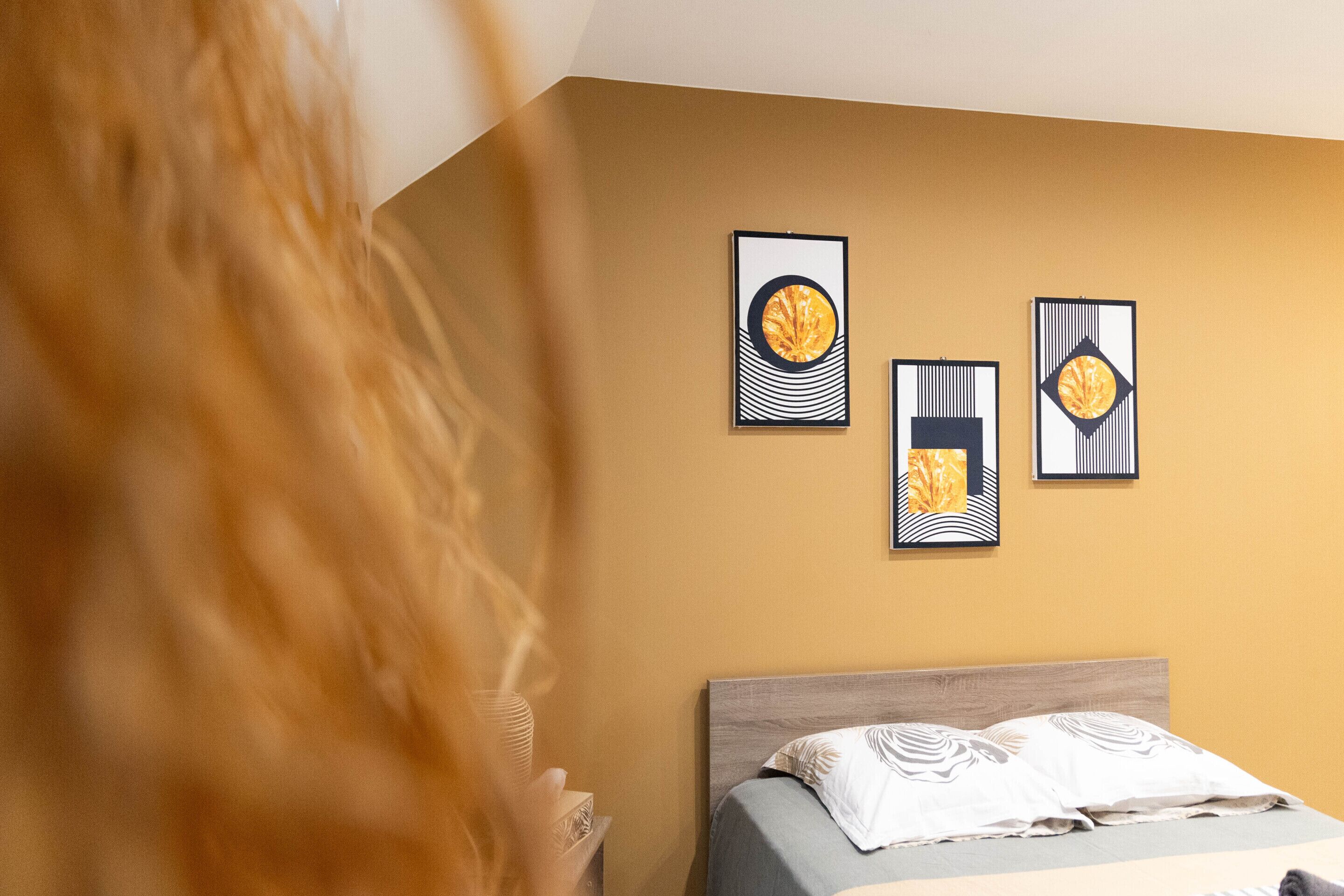 A bedroom with a bed, a nightstand, and three framed artworks on the wall.