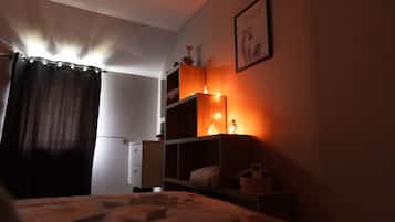 Un dormitorio con poca luz, una cama, un aparador y una estantería con adornos.