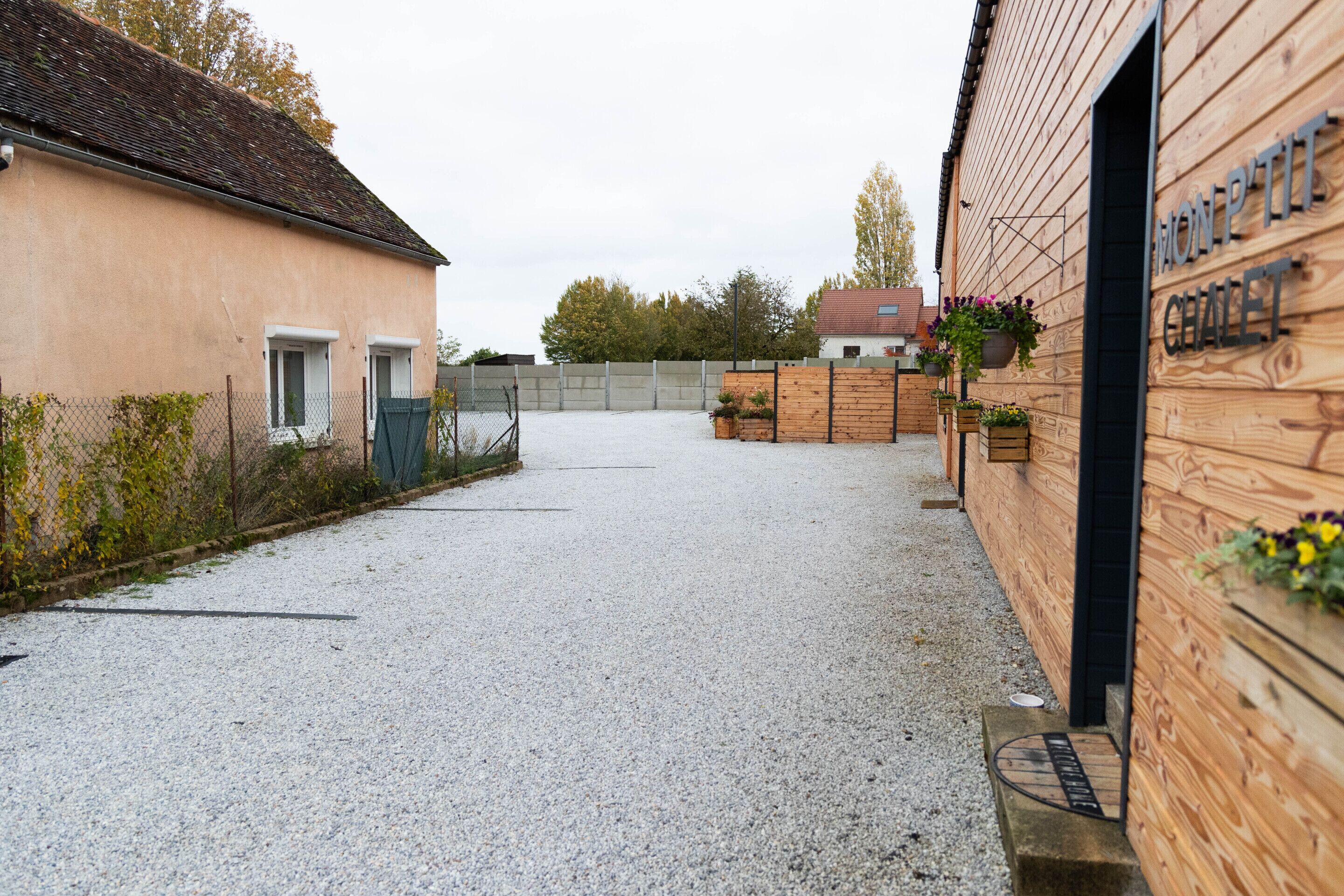 Ein Schotterweg führt zu einem Gebäude mit Holzfassade und einem Schild mit der Aufschrift 'MON P'TIT CHALET'.