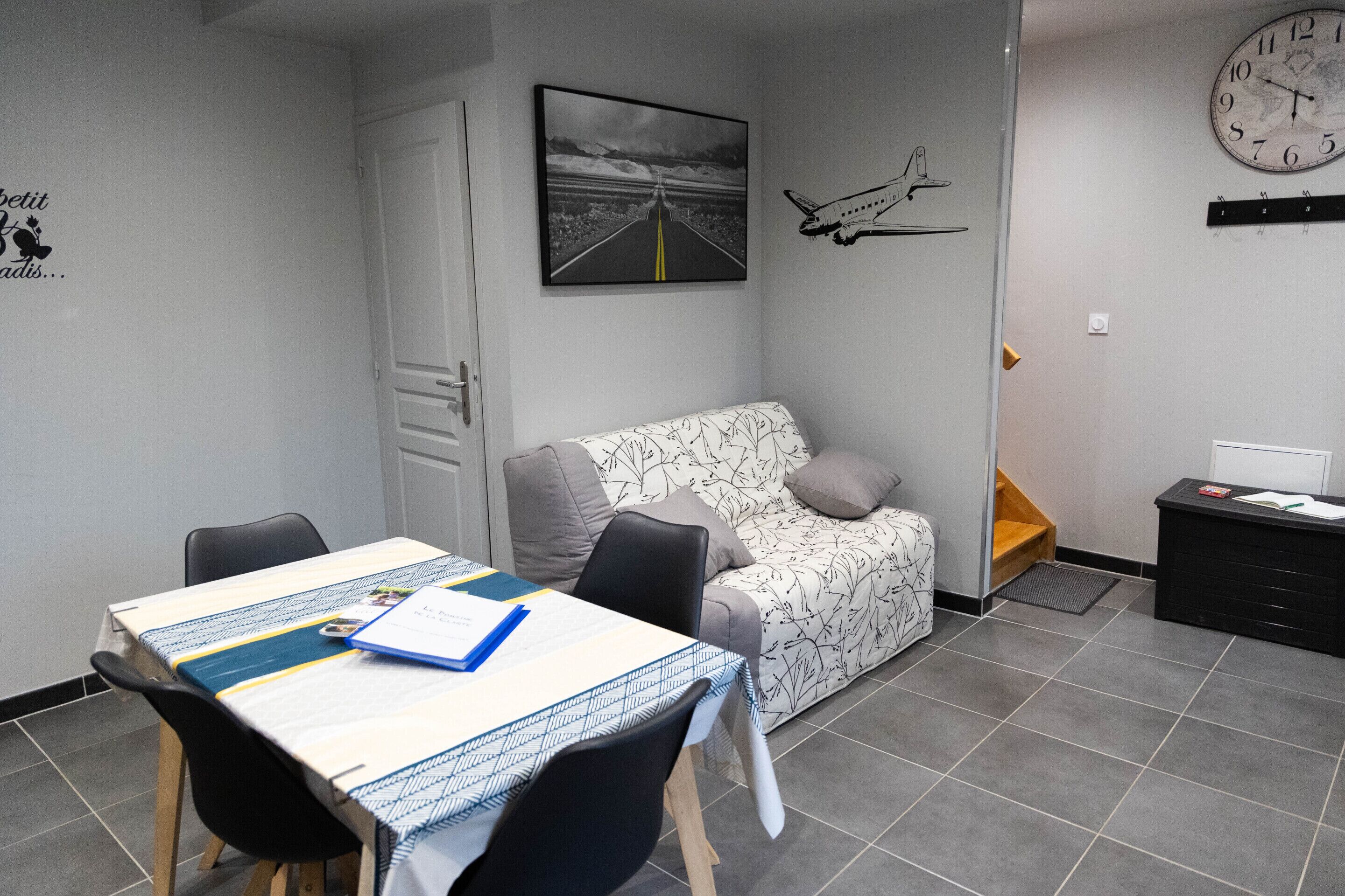 Ein kleiner, moderner Raum mit Esstisch, einer Couch, einer Uhr und einem gerahmten Bild an der Wand.