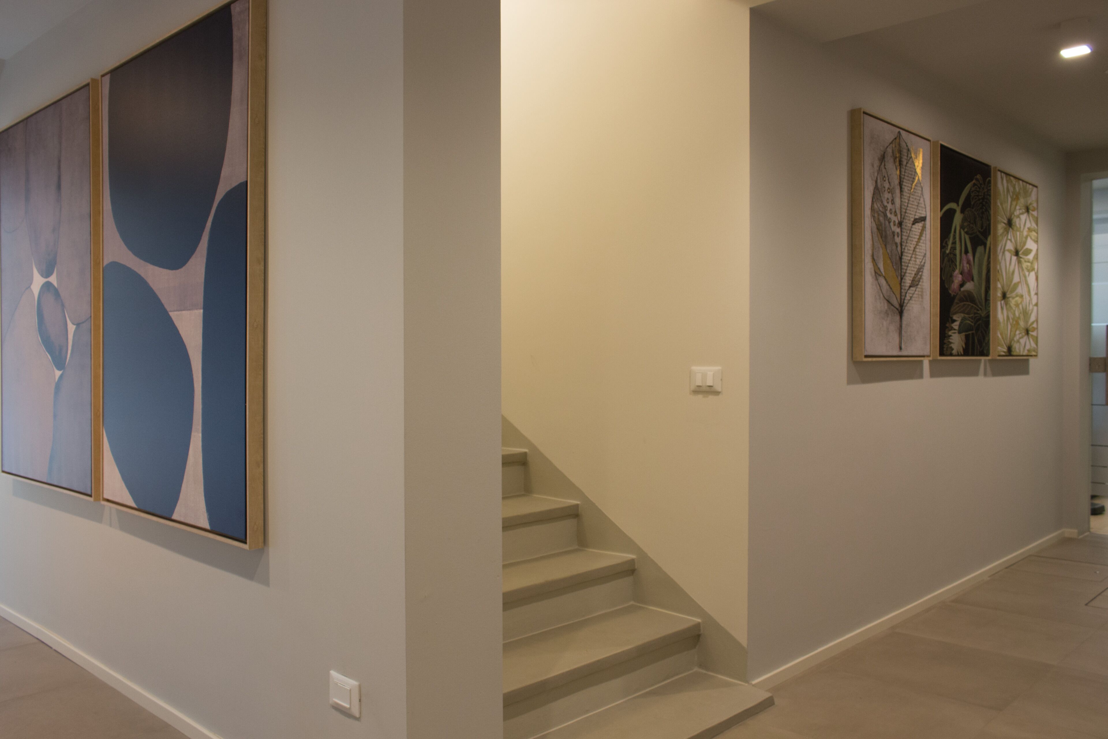 Un couloir avec un escalier et trois œuvres d’art encadrées accrochées aux murs.
