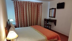 Une chambre d’hôtel avec un lit, un bureau avec une lampe, une chaise, une télévision et un miroir.