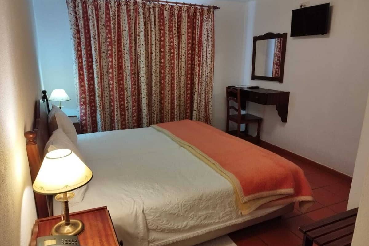 Une chambre d’hôtel avec un lit, un bureau avec une lampe, une chaise, une télévision et un miroir.