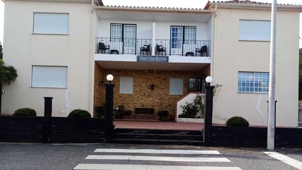 Een hotel met een gebouw van twee verdiepingen, een balkon met stoelen en een zebrapad ervoor.