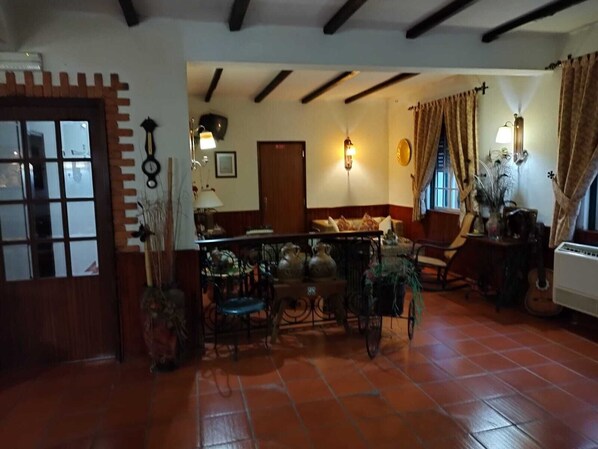 Una sala de estar acogedora con suelo de baldosas, un banco de madera, una mesa con sillas y una ventana con cortinas.