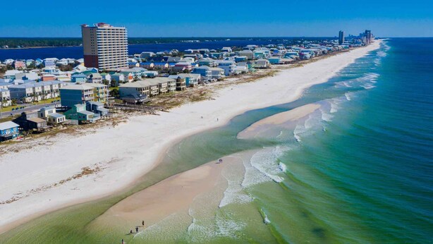 A coastal town with a long sandy beach, a high-rise building, and a city skyline in the distance. - Seas The Day @ West Side Cottages | Community Pool (Gulf Shores)