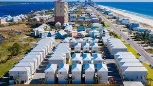A coastal area with a row of white buildings with blue roofs, a tall building with a red roof, and a beach in the background. - Seas The Day @ West Side Cottages | Community Pool (Gulf Shores)