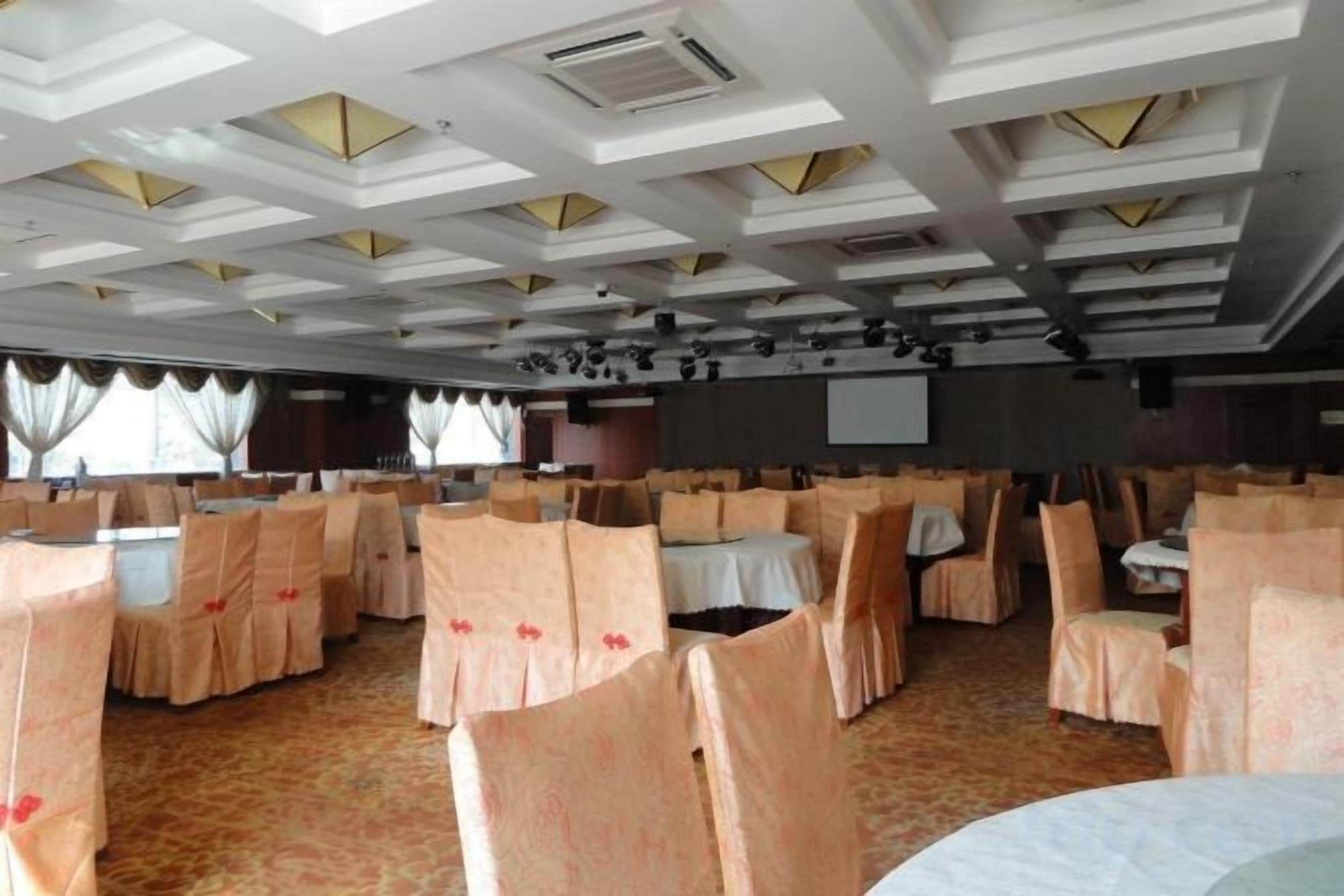 A banquet hall with round tables and chairs, a stage, and a projection screen.
