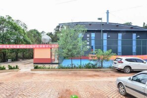 A building with a curved roof, a satellite dish, and a red and yellow sign. There are trees and a paved area with cars parked.