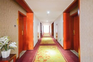Pasillo de hotel con pisos alfombrados, puertas de madera y una planta en maceta.