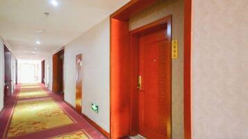 A hotel corridor with carpeted floors, wooden doors, and a visible emergency exit sign.