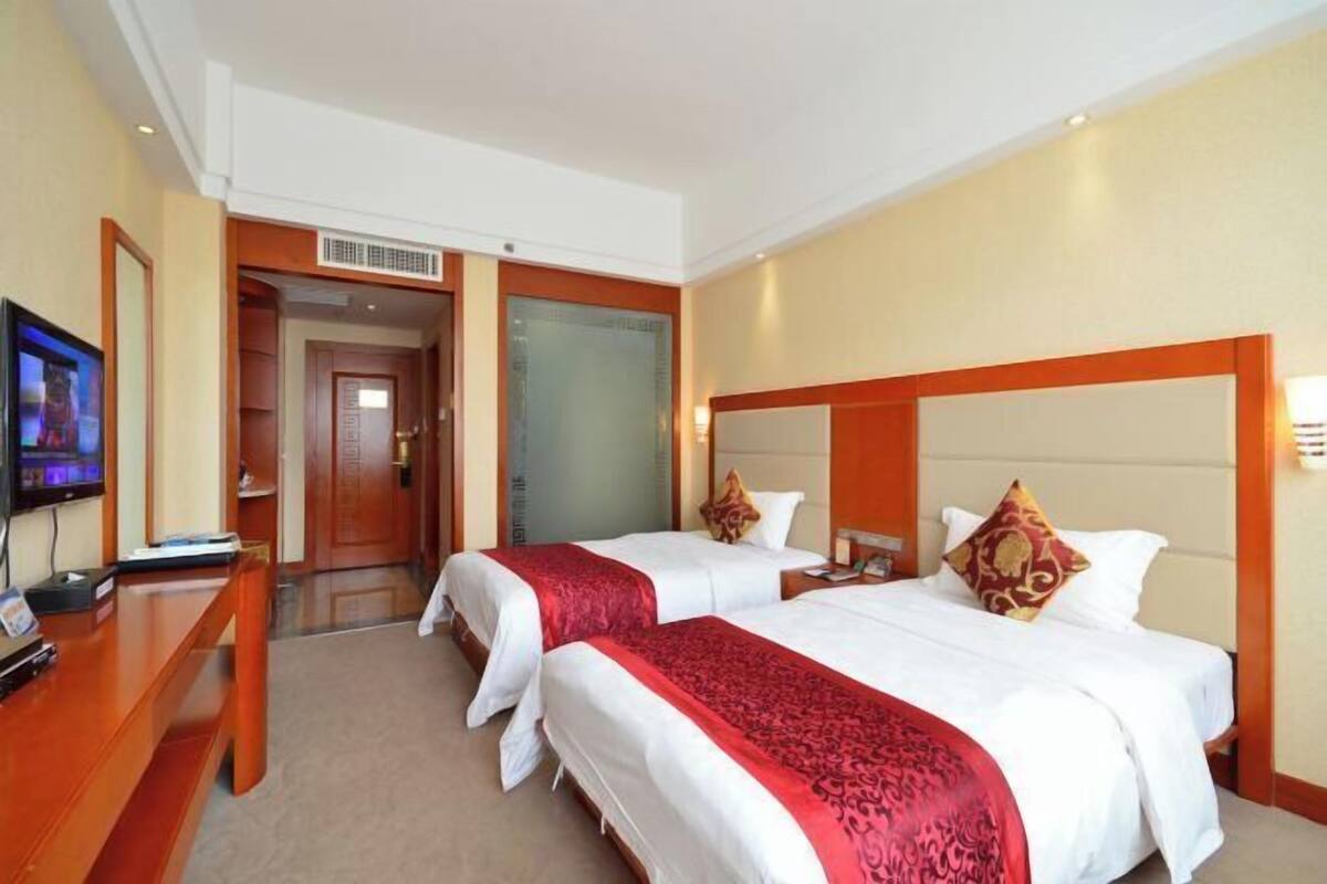 Habitación de hotel con dos camas, un escritorio, un televisor y una puerta de cristal que da a otra habitación.