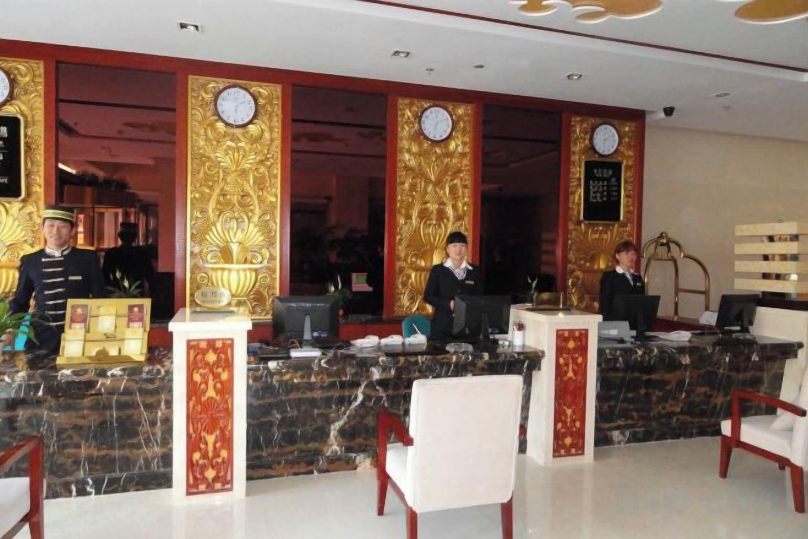Zona de recepción de un hotel con mostrador de mármol, recepcionistas y un reloj en la pared.
