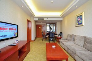 Une chambre d’hôtel équipée d’une télévision, d’un canapé, d’une table basse et d’un coin repas avec des chaises et une table.