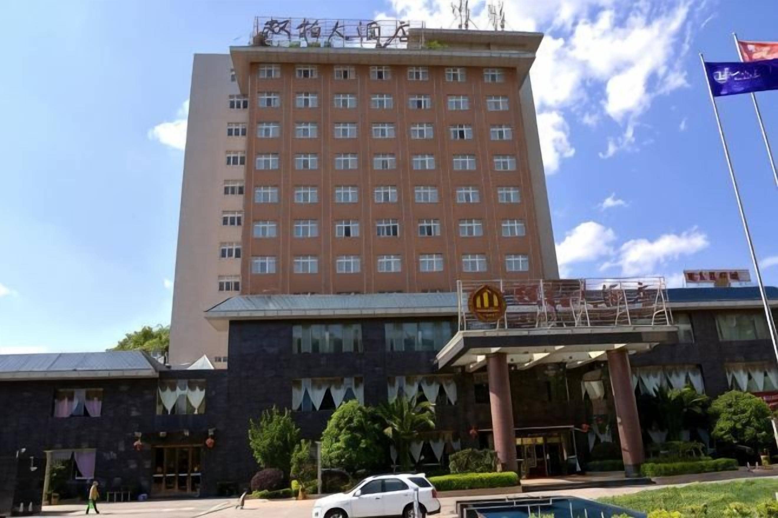 A multi-story hotel with a prominent entrance, a flag, and a parking area.
