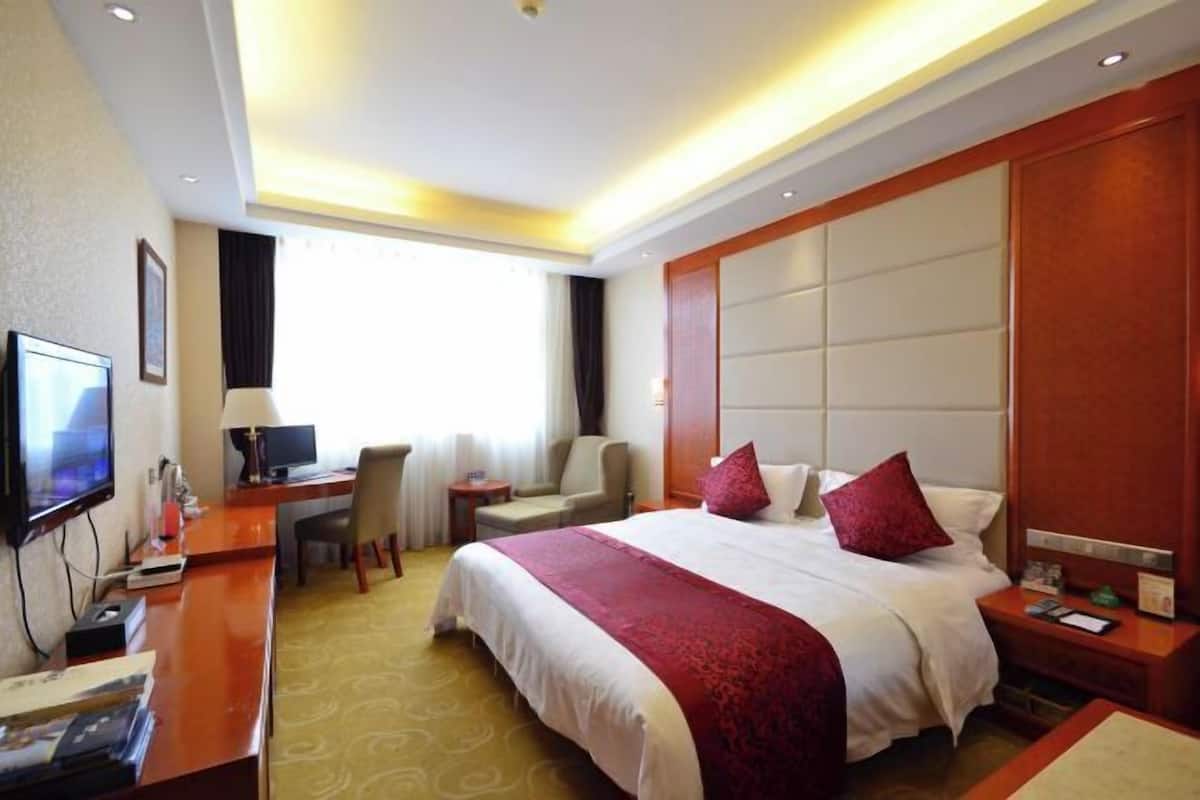 Una habitación de hotel con cama, escritorio, silla, televisor y un ventanal grande.