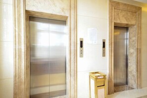 Dos puertas de ascensor en un pasillo con una pared de mármol y una pequeña mesa de madera.